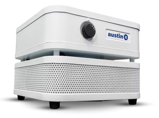 The Austin “it” Air Purifier is a white, box-shaped unit with a perforated lower section, a front control knob, and features the blue Austin “it” logo on the upper front panel.