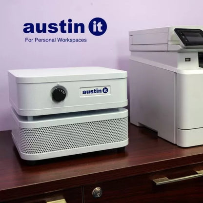 A white Austin “it” Air Purifier sits on a wooden desk next to a printer, with the Austin “it” logo and “For Personal Workspaces” on the wall behind, highlighting how the air purifier fits seamlessly into any workspace.